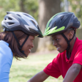 A mother and son smile at each other while wearing bike helmets.