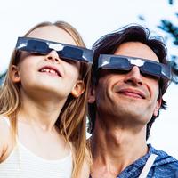 A father and daughter look up to the sky as they wear protective shade to protect their eyes from the sun.  