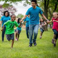 Kids run in a field along with their camp counselor.