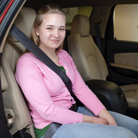 A teen safety sits in a car with their seat belt on securely. 