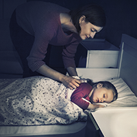 little girl sleeping in bed while mom tucks her in