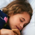 A young girl takes a nap as she cuddles with her teddy bear. 