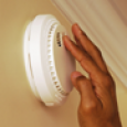 A hand reaches to check a smoke alarm.