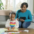 A child colors as her mother looks on with a smile.