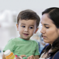 A mother reads the label of a medication bottle while holding her child.